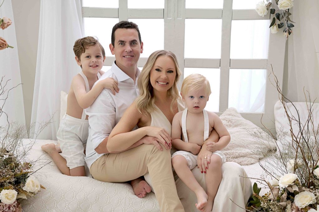 Família sorridente em ensaio fotográfico no Estúdio e Cia em Curitiba, com pais e dois filhos em cenário claro e elegante.