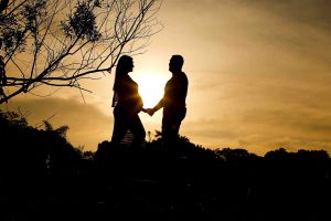 Casal em ensaio de gestante em Curitiba, em pé de frente um para o outro, de mãos dadas, com pôr do sol ao fundo.