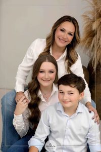 Mãe sorridente abraçada com seus dois filhos, transmitindo carinho e união familiar.